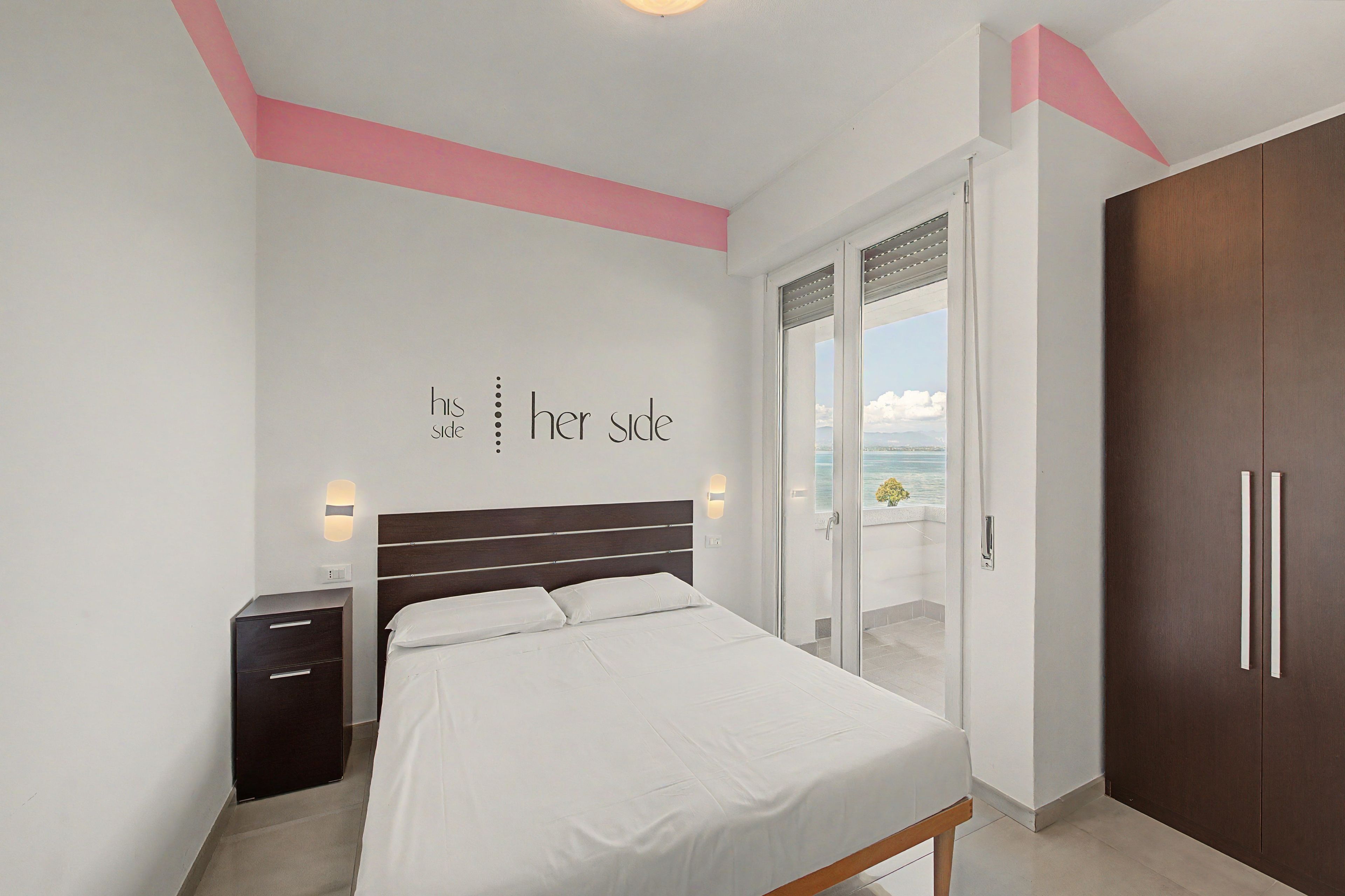 Ein Schlafzimmer mit Bett, Nachttisch, Kleiderschrank und einer Glastür, die auf einen Balkon mit Blick führt.