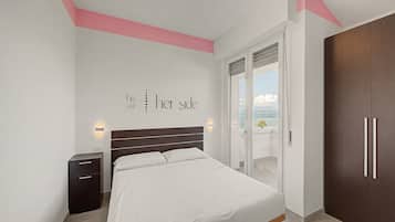 Ein Schlafzimmer mit Bett, Nachttisch, Kleiderschrank und einer Glastür, die auf einen Balkon mit Blick führt.