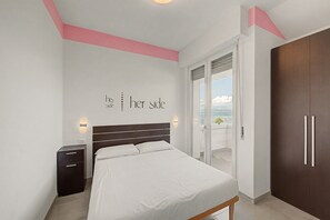 Une chambre à coucher comprenant un lit, une table de chevet, une armoire et une porte-fenêtre coulissante donnant sur un balcon avec vue.