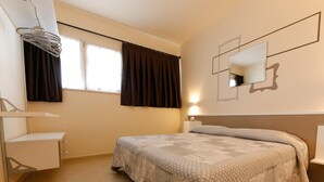 Quarto com cama, mesa de cabeceira, luminária pendente, janela com cortinas e espelho fixado na parede.