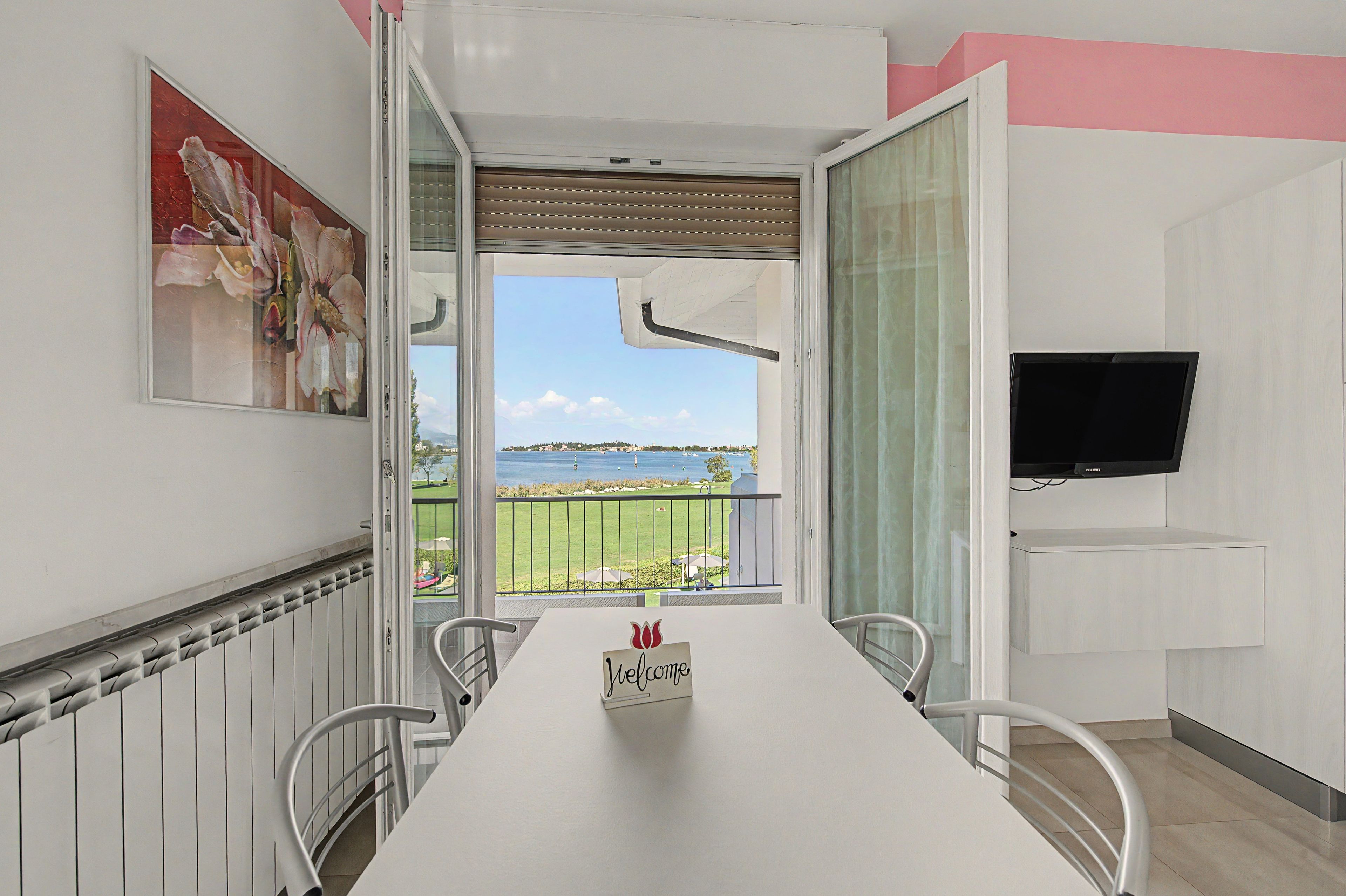 A room with a dining table, chairs, a television, and a view of a body of water.