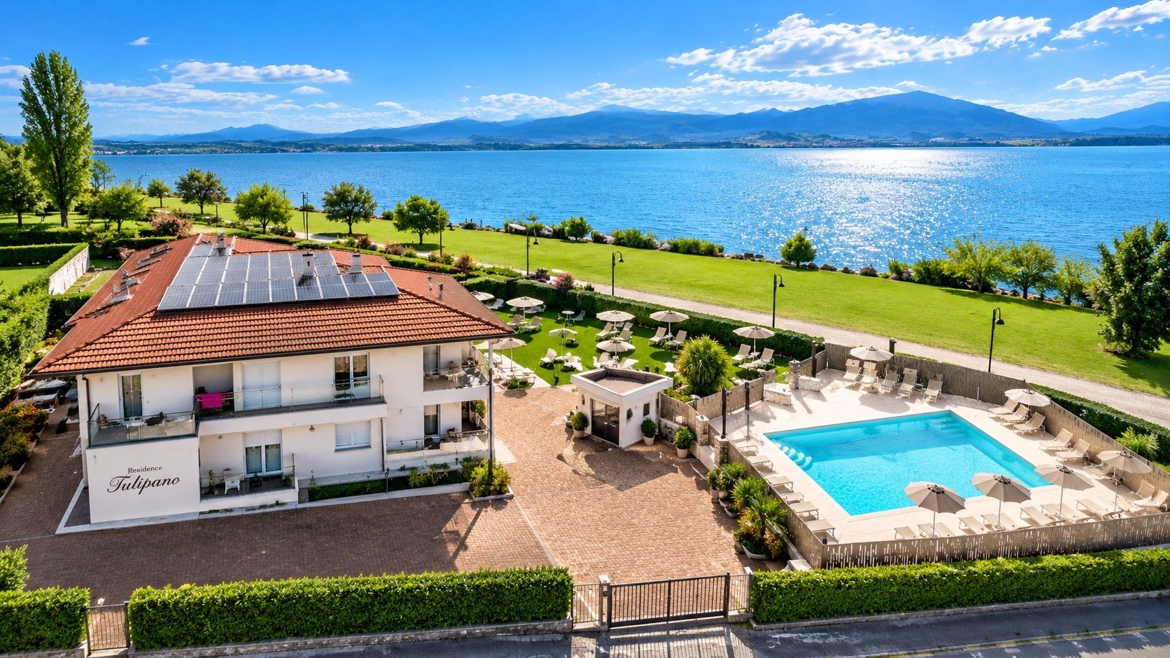 Un hotel con piscina, pannelli solari sul tetto e vista su un lago e montagne.