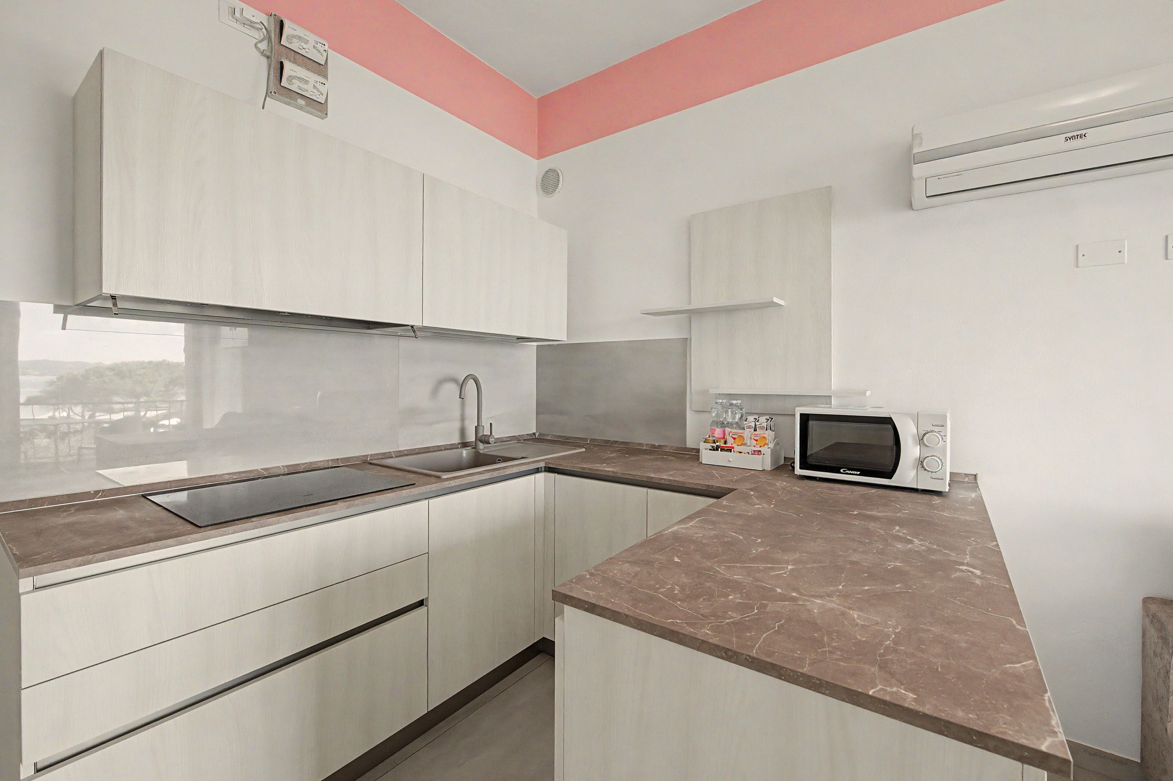 Cocina compacta con armarios blancos, pileta de acero inoxidable, microondas y horno integrado.