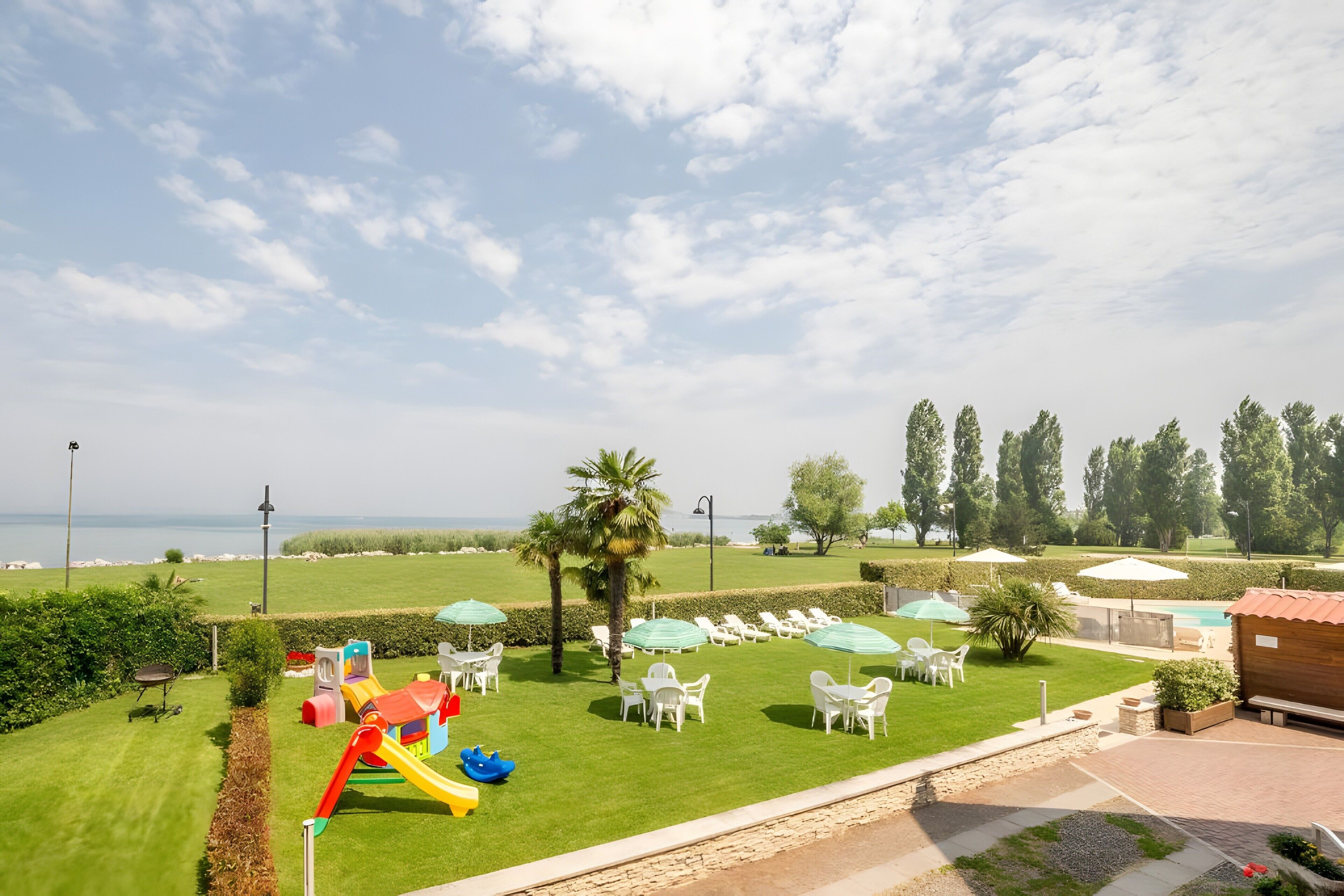 Un espacio exterior soleado con zona de juegos infantiles, mobiliario y vistas al mar.