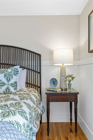A bedroom with a bed, a bedside table with a lamp, and a vase with flowers.