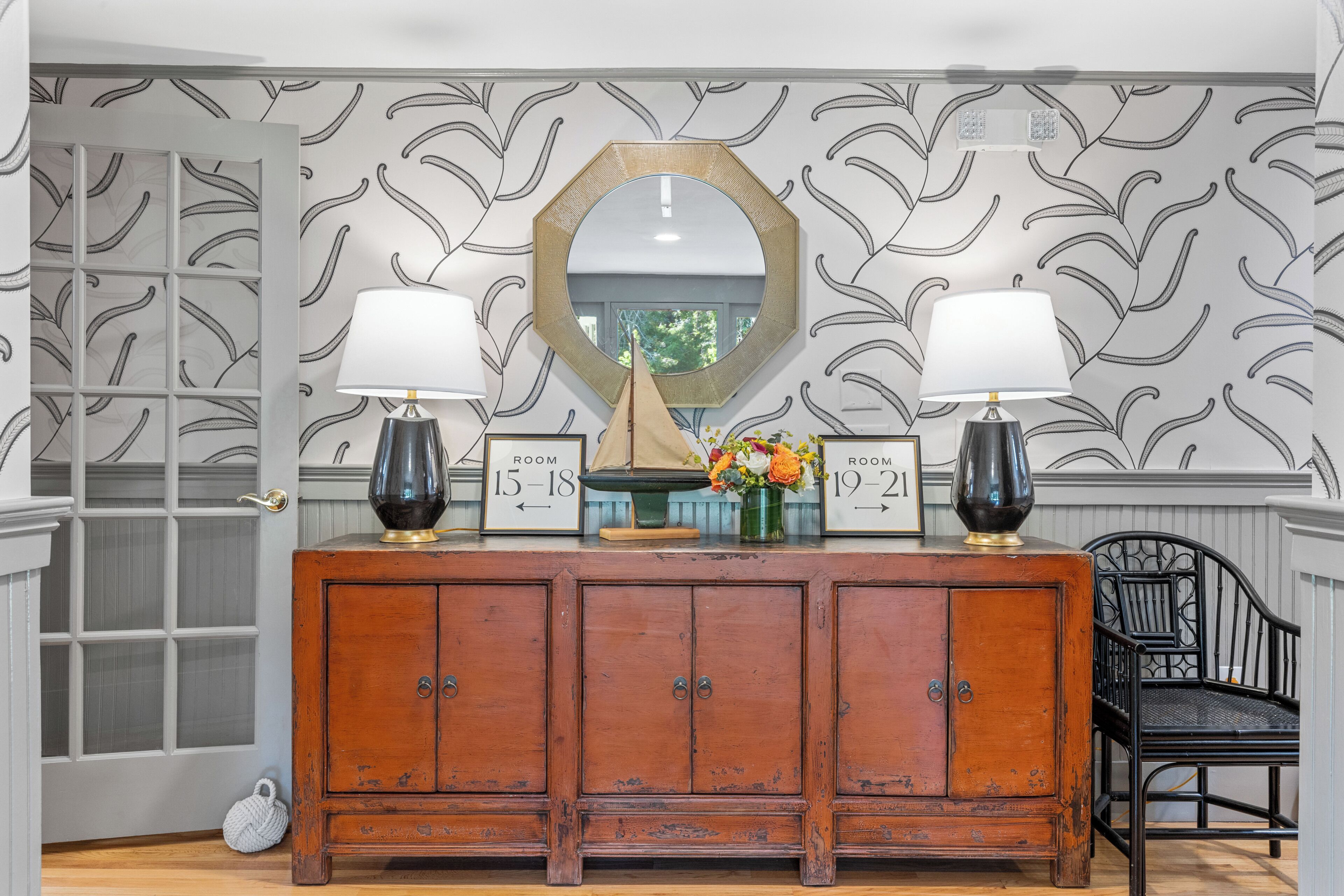 A wooden cabinet with two lamps, a mirror, and room number signs.