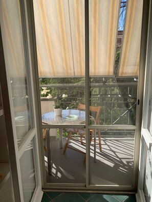 A sliding glass door leading to an outdoor balcony with a round table and chairs, a potted plant, and a view of a building with a balcony. - Spacious apartment in the historic center of Fondi (Fondi)