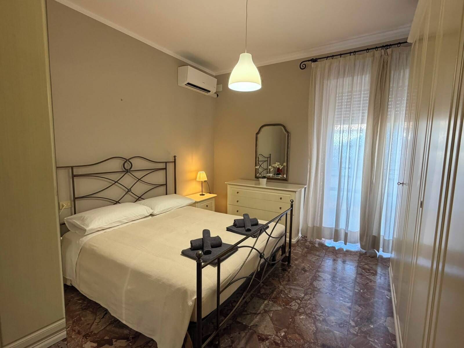 Una camera da letto con un letto, lampada da comodino, comò, specchio e condizionatore d'aria.