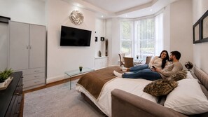 A bedroom with a bed, a TV mounted on the wall, a wardrobe, and a window with blinds. - Ground floor, Private, Free Parking, Park, Views (Liverpool)