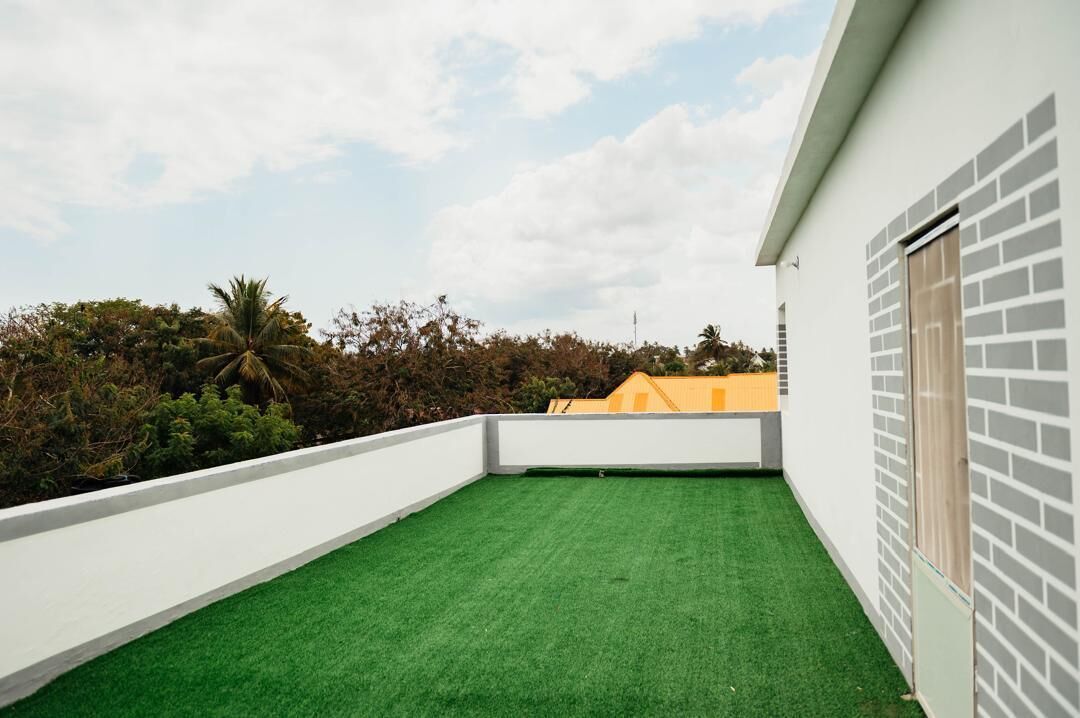 Terraço com grama sintética, parede branca e área de tijolos.