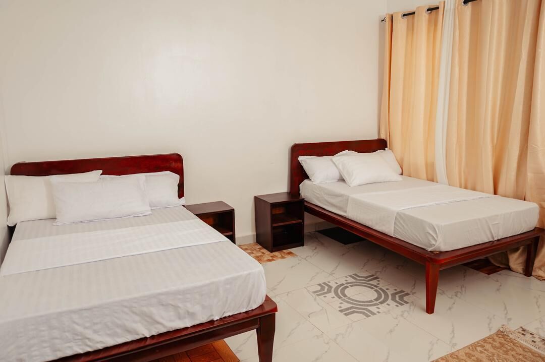 Quarto de hotel com duas camas de solteiro, mesa de cabeceira e um tapete estampado.