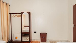 Quarto de hotel com cama, guarda-roupa com espelho, pequena lixeira e tapete estampado.
