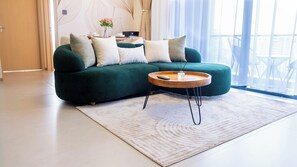 A modern living room with a green sofa, a round wooden coffee table, and a white rug. - 2BR with 180° Skyline Views | Pool & Gym (Nairobi)