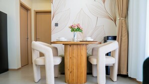 Une pièce moderne avec une table ronde en bois, deux chaises blanches, un vase avec des fleurs et un mur orné d’un motif de feuilles.