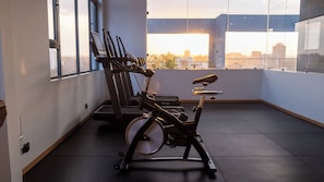 Ein Fitnessstudio mit Ergometer und Laufband, große Fenster mit Blick auf die Stadt und ein modernes architektonisches Design.
