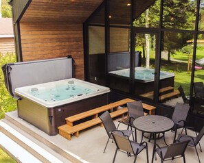 Un bain à remous avec des bancs et des chaises en bois, un patio fermé par des baies vitrées et une vue sur la verdure environnante.