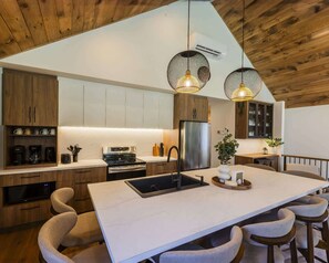 Une cuisine moderne dotée d’un îlot central, de meubles en bois, d’appareils électroménagers en acier inoxydable et de luminaires suspendus.