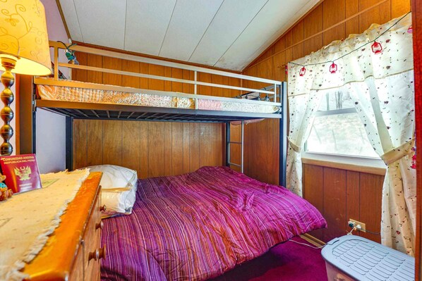 A bunk bed room with a window, a desk, and a lamp.