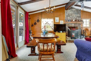 A cozy room with a wooden table, benches, a television, a fireplace, and a stone wall.