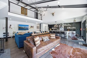 Ein modernes Wohnzimmer mit einem braunen Ledersofa, einem blauen Sofa und einem Essbereich, im Hintergrund befindet sich eine Küche.