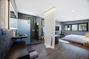 Een moderne slaapkamer met een groot bed, een nachtkastje, een televisie en een badkamer met douche en wastafel.