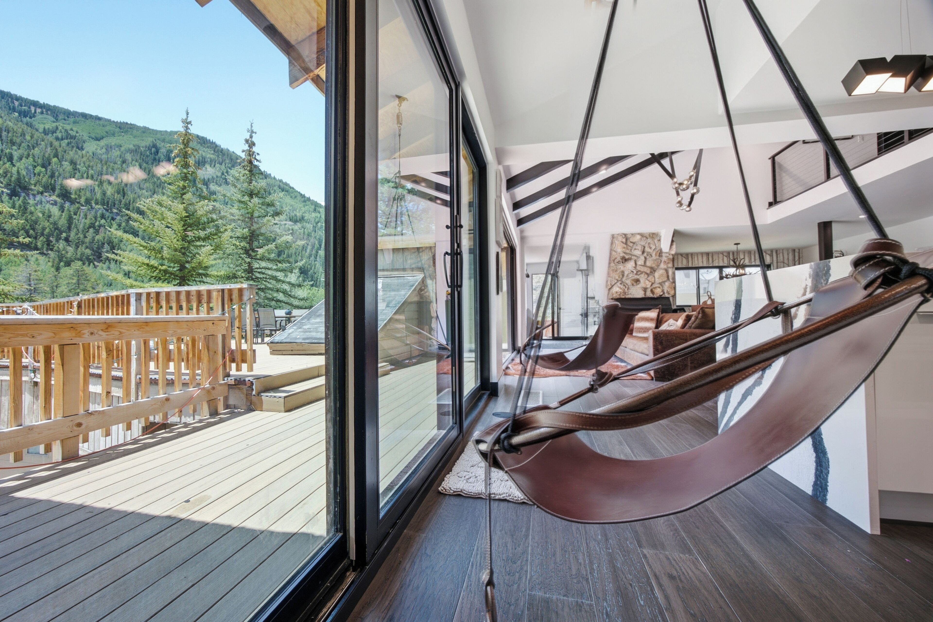 A hammock in a room with a view of a wooden deck and forested hills.