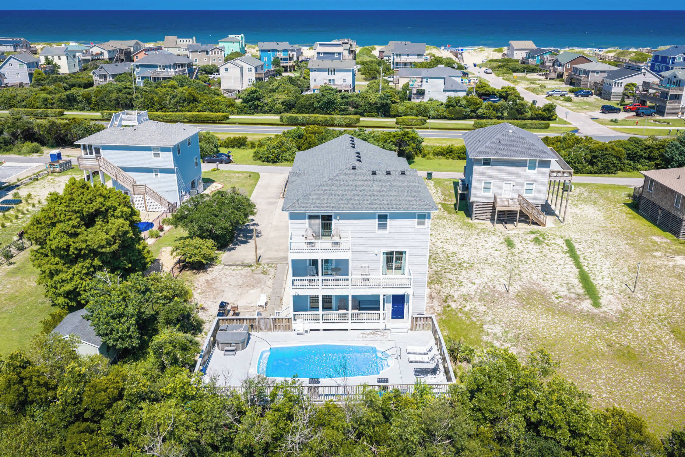 A multi-story residential building with a swimming pool, surrounded by greenery and a beach view.