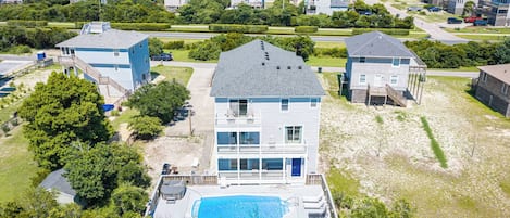 A multi-story residential building with a swimming pool, surrounded by greenery and a beach view.