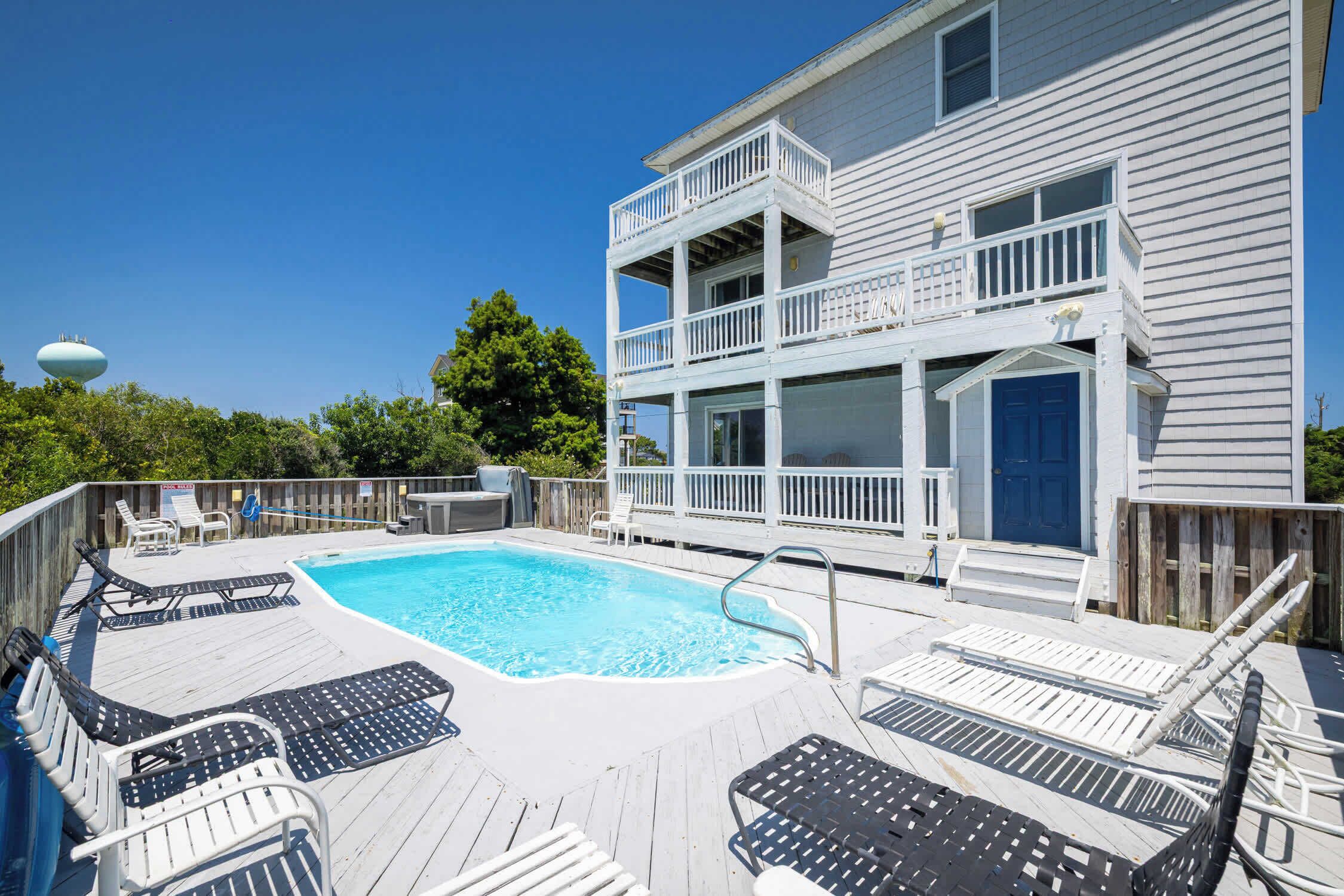 A two-story building with a swimming pool, deck chairs, and a blue door.
