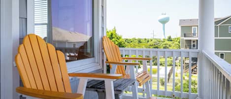 A porch with wooden chairs and a table, overlooking a residential area with houses and a water tower.