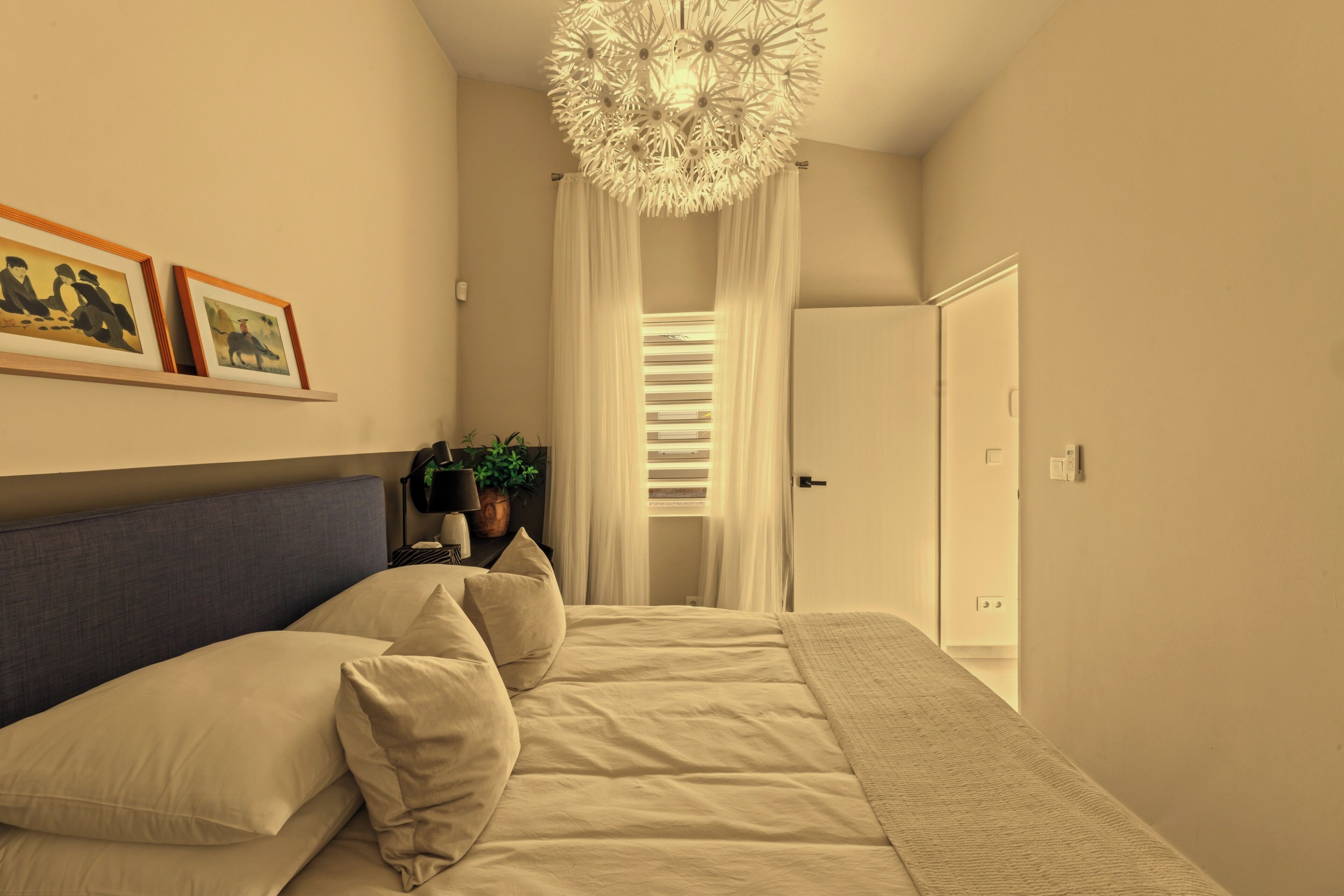 A bedroom with a bed, a headboard, a chandelier, a door, and a wall with framed artwork.