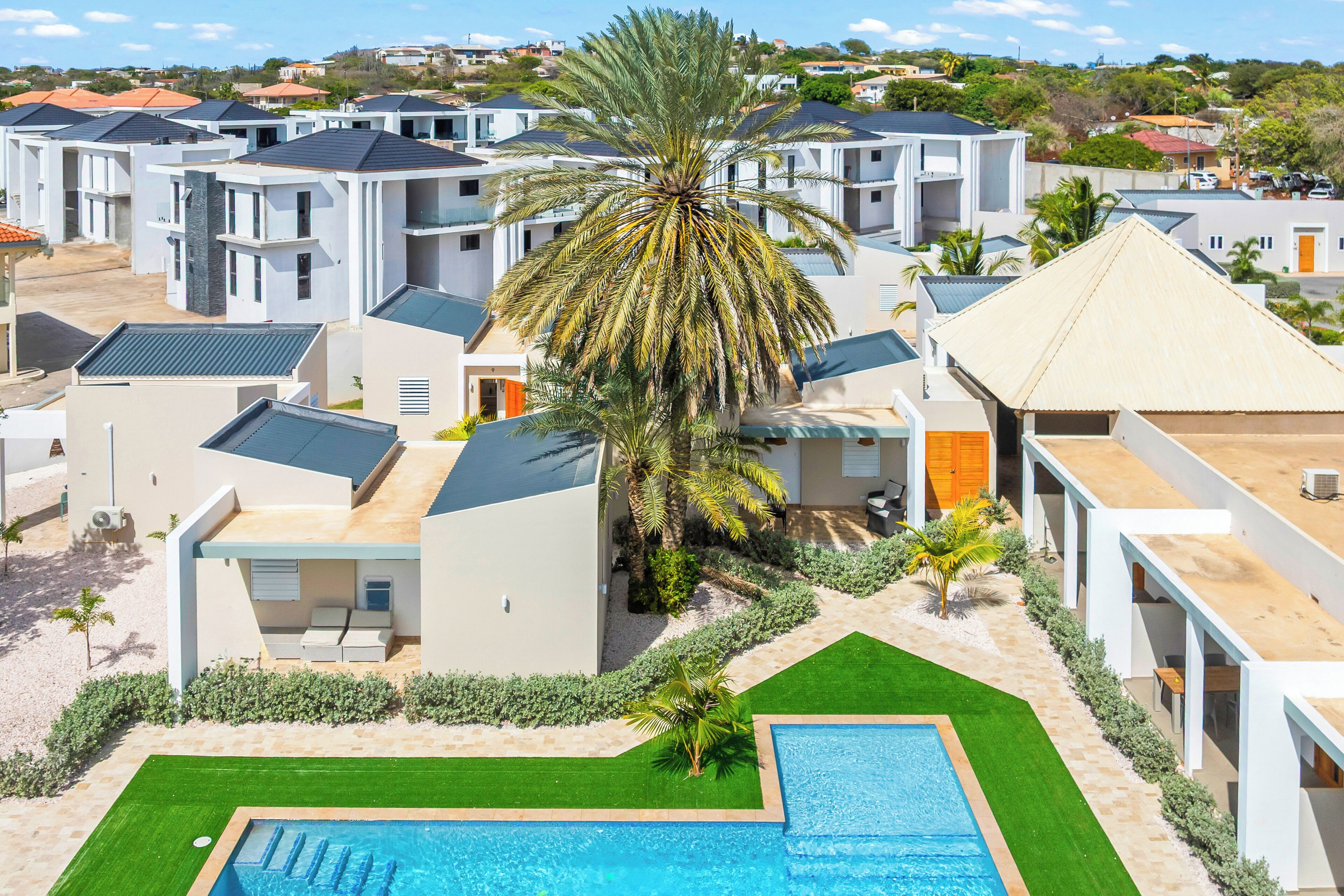 A modern residential area with multiple houses, a swimming pool, and palm trees.