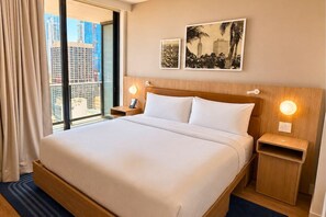 Habitació d'hotel amb un llit gran, dues taules de nit, una finestra amb cortines i dues làmpades murals.