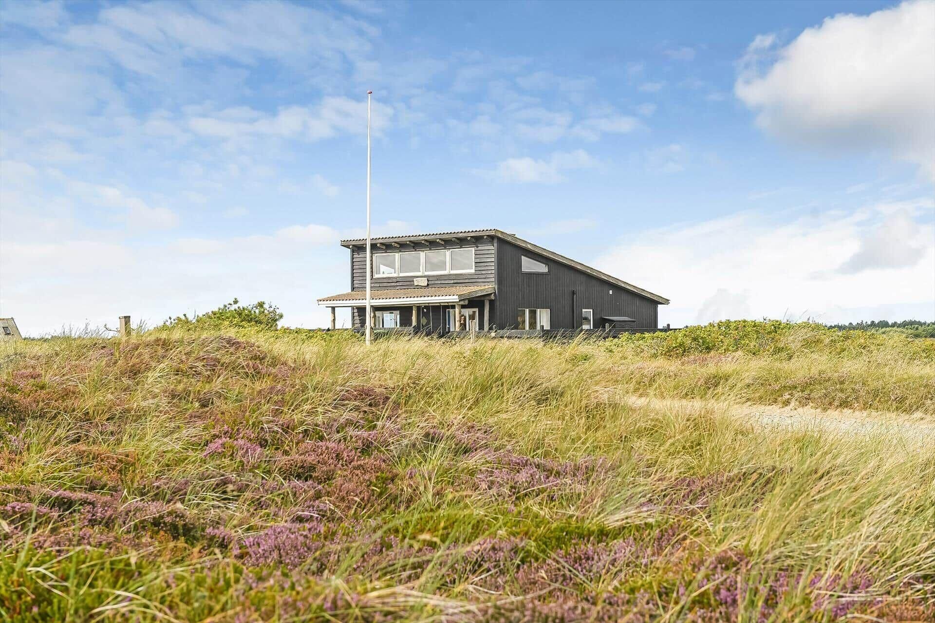 Un bâtiment moderne à deux étages, doté d’un toit plat, situé sur une colline herbeuse où la végétation est clairsemée.