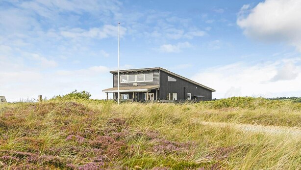 Een modern gebouw met twee verdiepingen en een plat dak, gelegen op een grasheuvel met weinig beplanting.