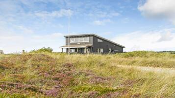 Un bâtiment moderne à deux étages, doté d’un toit plat, situé sur une colline herbeuse où la végétation est clairsemée.