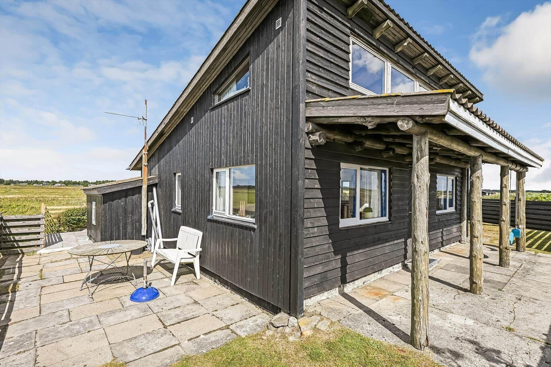 Une maison en bois à deux étages, dotée d’un porche abrité, d’un petit patio avec une table et une chaise, et offrant une vue sur le paysage environnant.
