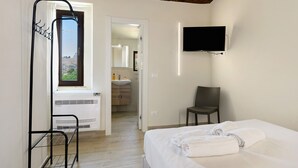 A hotel room with a bed, a chair, a TV, a bathroom with a sink, and a window with a view of the outdoors. - A Schietta Room – Sikania Agrirelais, Mountain View (Caccamo)