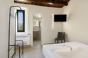 Ett hotellrum med en säng, en stol, en tv, ett badrum med handfat och ett fönster med utsikt över omgivningen.