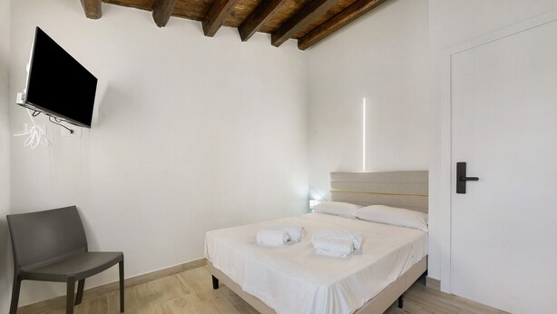 A hotel room with a bed, a chair, a flat-screen TV mounted on the wall, and a door. - A Schietta Room – Sikania Agrirelais, Mountain View (Caccamo)