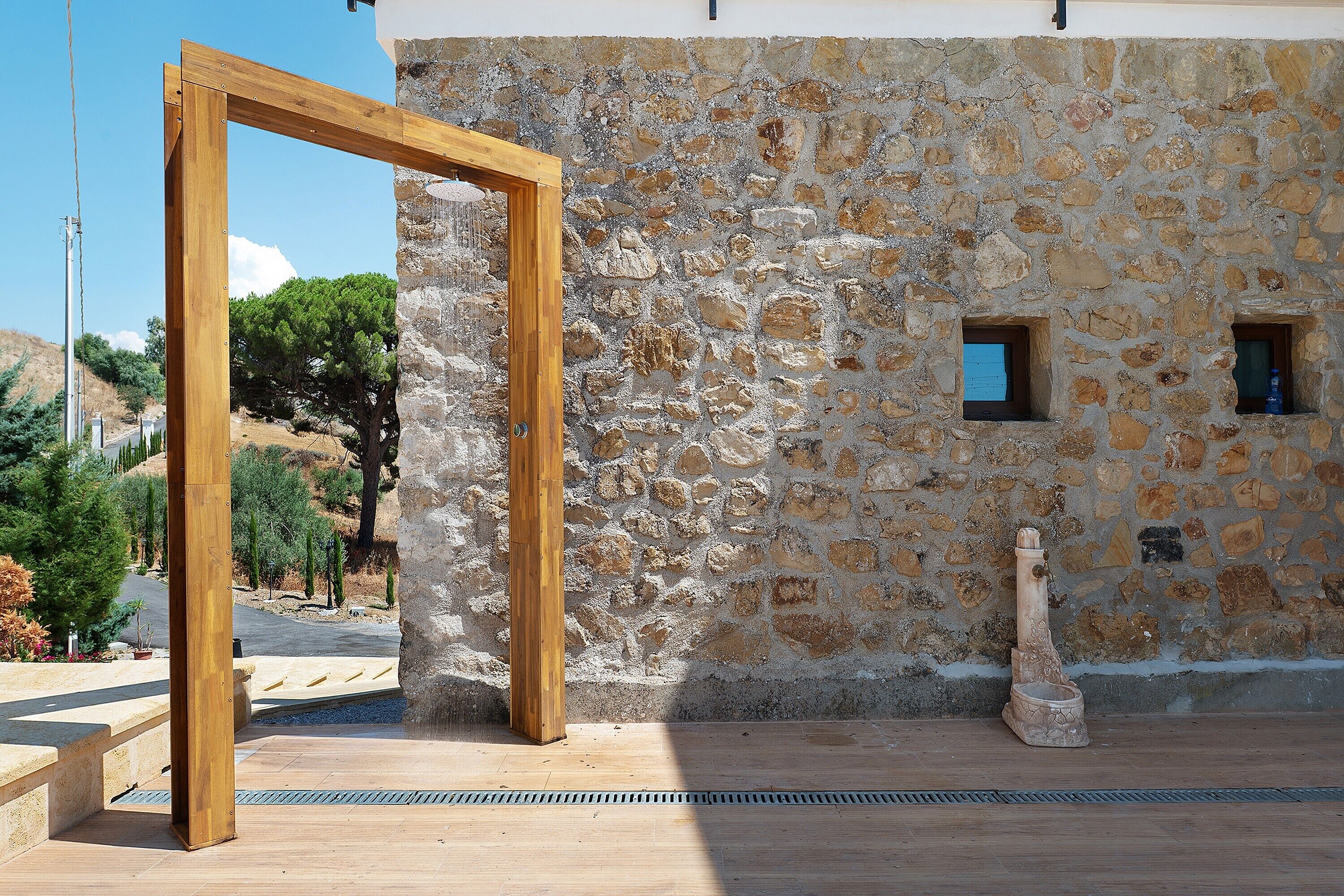 A stone wall with a wooden frame structure, a small window, and a water feature.