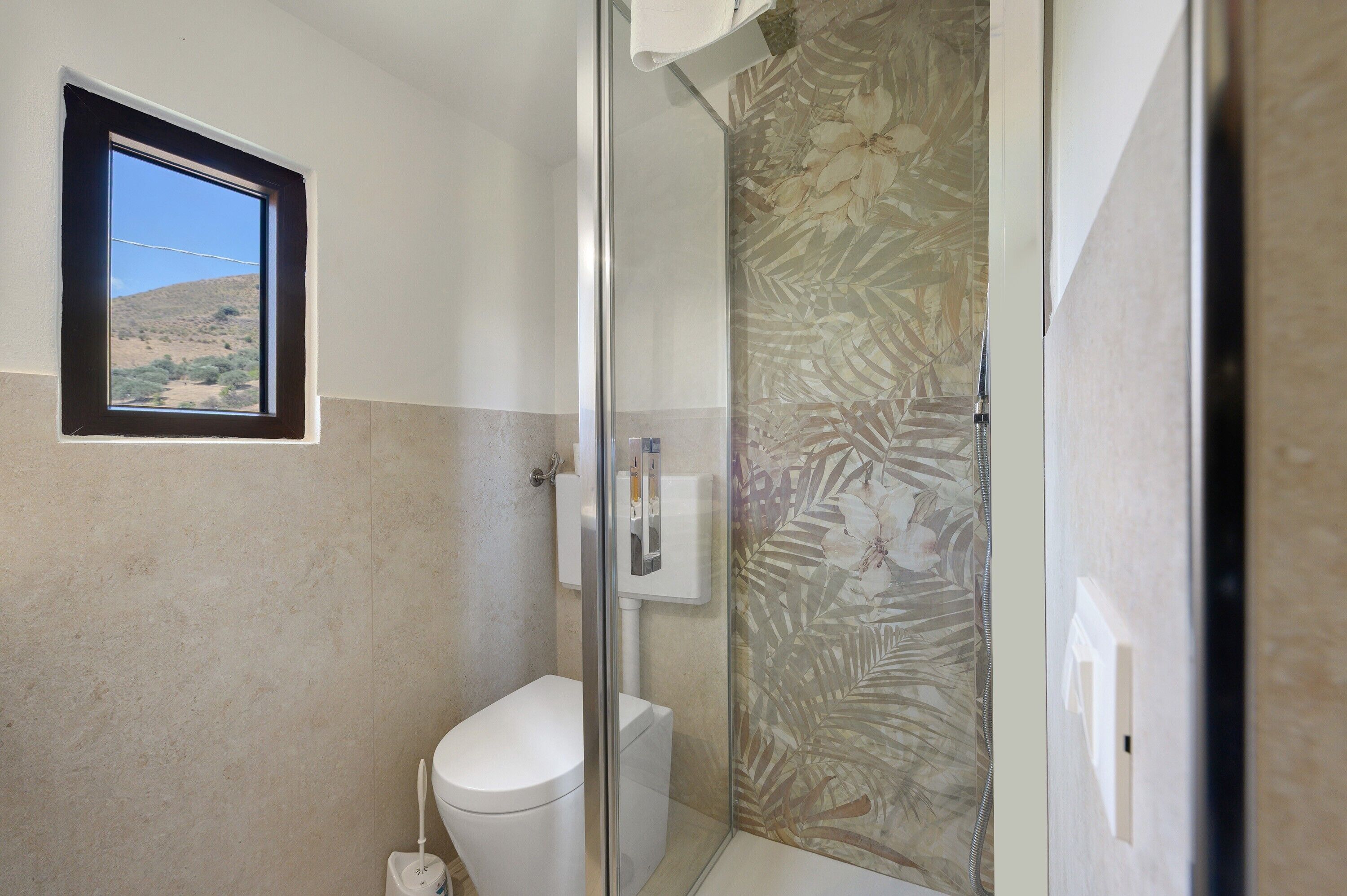 Ein Badezimmer mit Toilette, einer Duschkabine aus Glas und einem Fenster mit Blick auf eine Wüstenlandschaft.