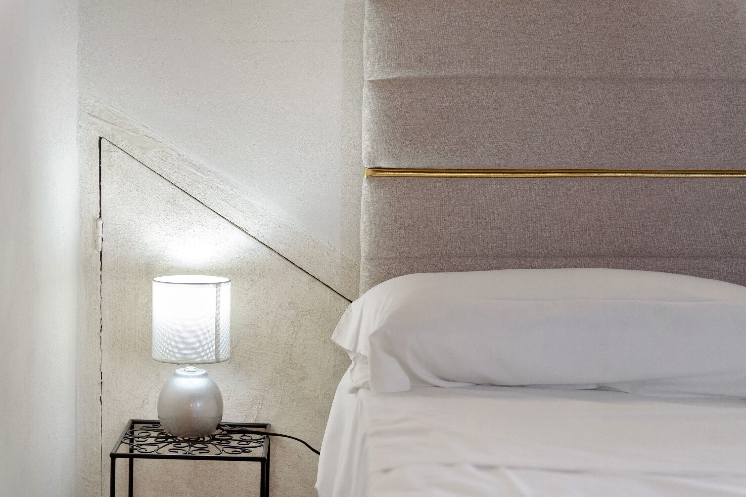 A neatly made bed with white linens, a bedside lamp, and a small table with a vase.