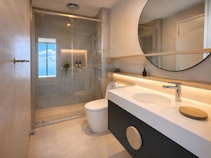 A modern bathroom with a glass-enclosed shower, a toilet, a sink with a mirror, and a view of the sky. - Sage Above the Sea - Ocean Views (Broadbeach)