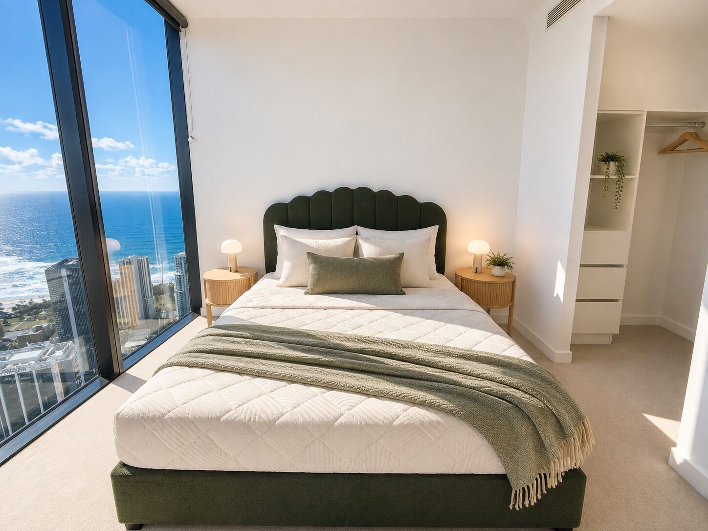 A modern bedroom with a large bed, two bedside tables, a view of the ocean, and a walk-in closet.