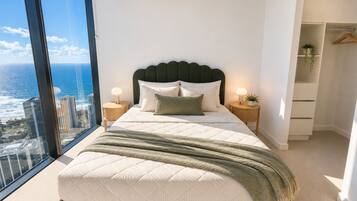 A modern bedroom with a large bed, two bedside tables, a view of the ocean, and a walk-in closet.