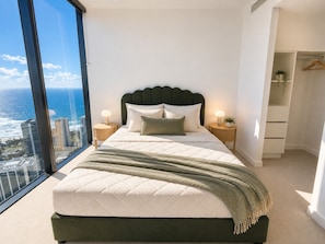 A modern bedroom with a large bed, two bedside tables, a view of the ocean, and a walk-in closet. - Sage Above the Sea - Ocean Views (Broadbeach)