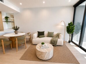 A modern living room with a sofa, a round coffee table, and a dining area with chairs and a table. - Sage Above the Sea - Ocean Views (Broadbeach)
