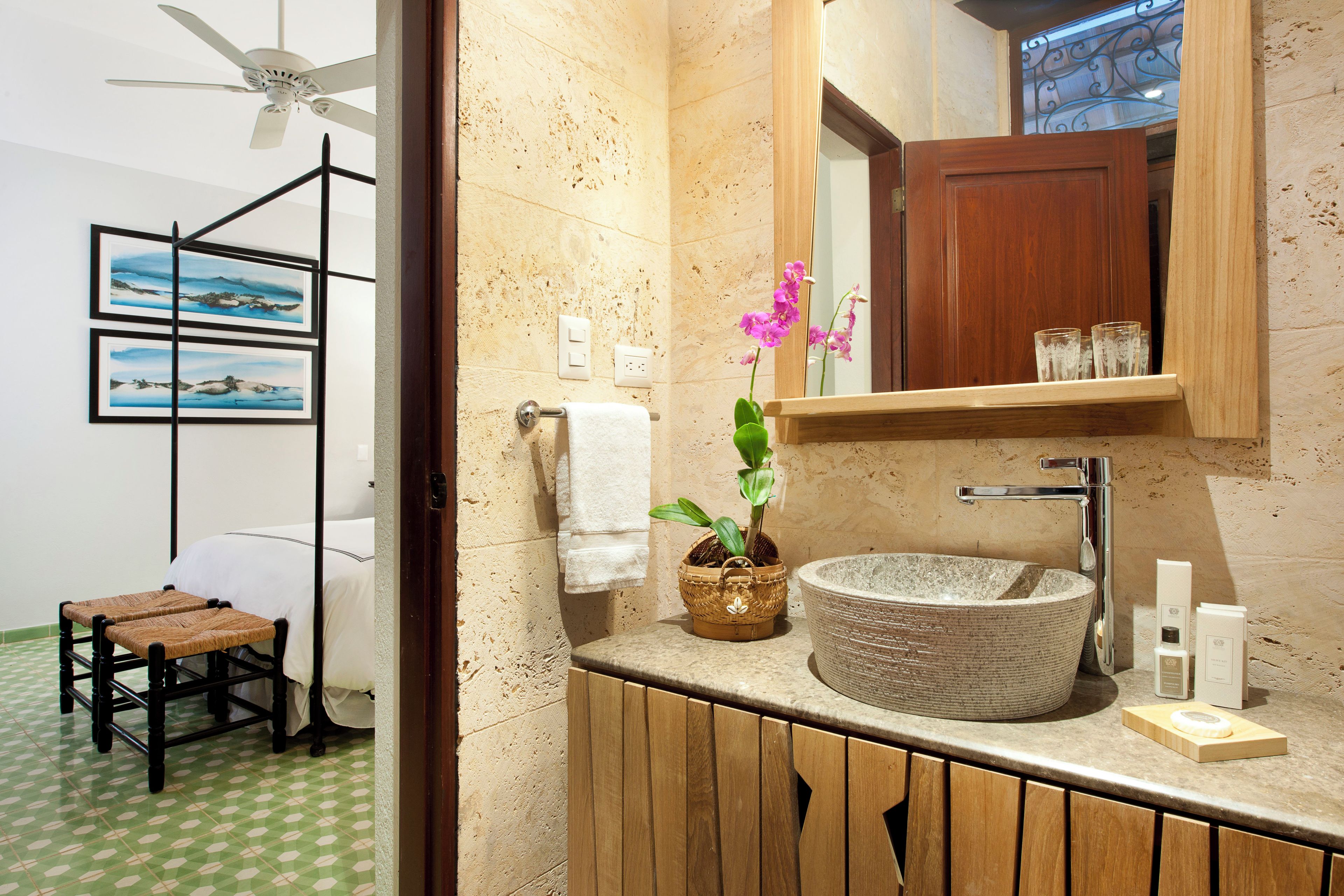 Un baño con un lavamanos grande tipo tazón, un mueble de madera, un espejo, un ventilador de techo y una pequeña mesa con una silla.