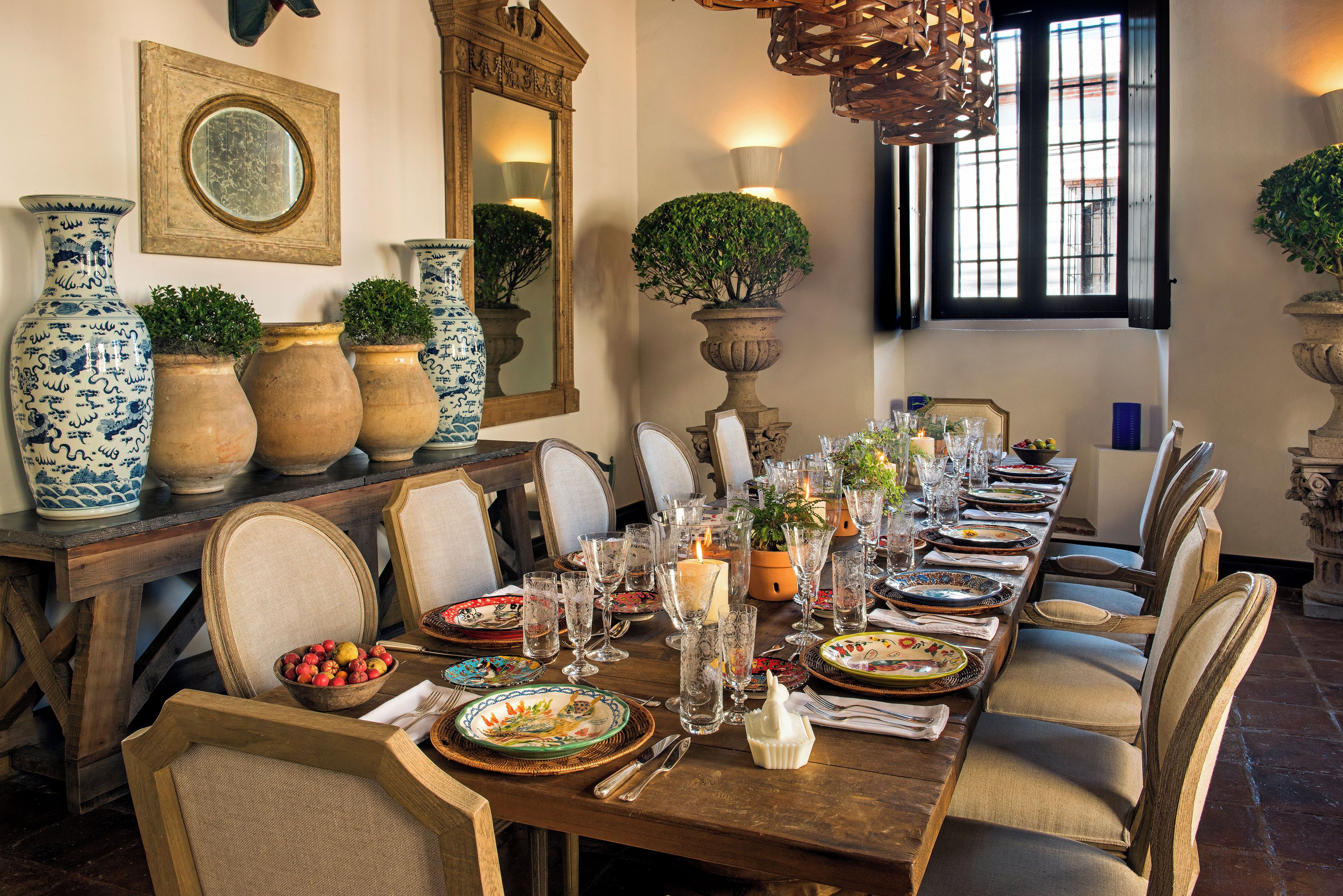 Uma sala de jantar com uma mesa de madeira comprida posta para uma refeição, rodeada de cadeiras.